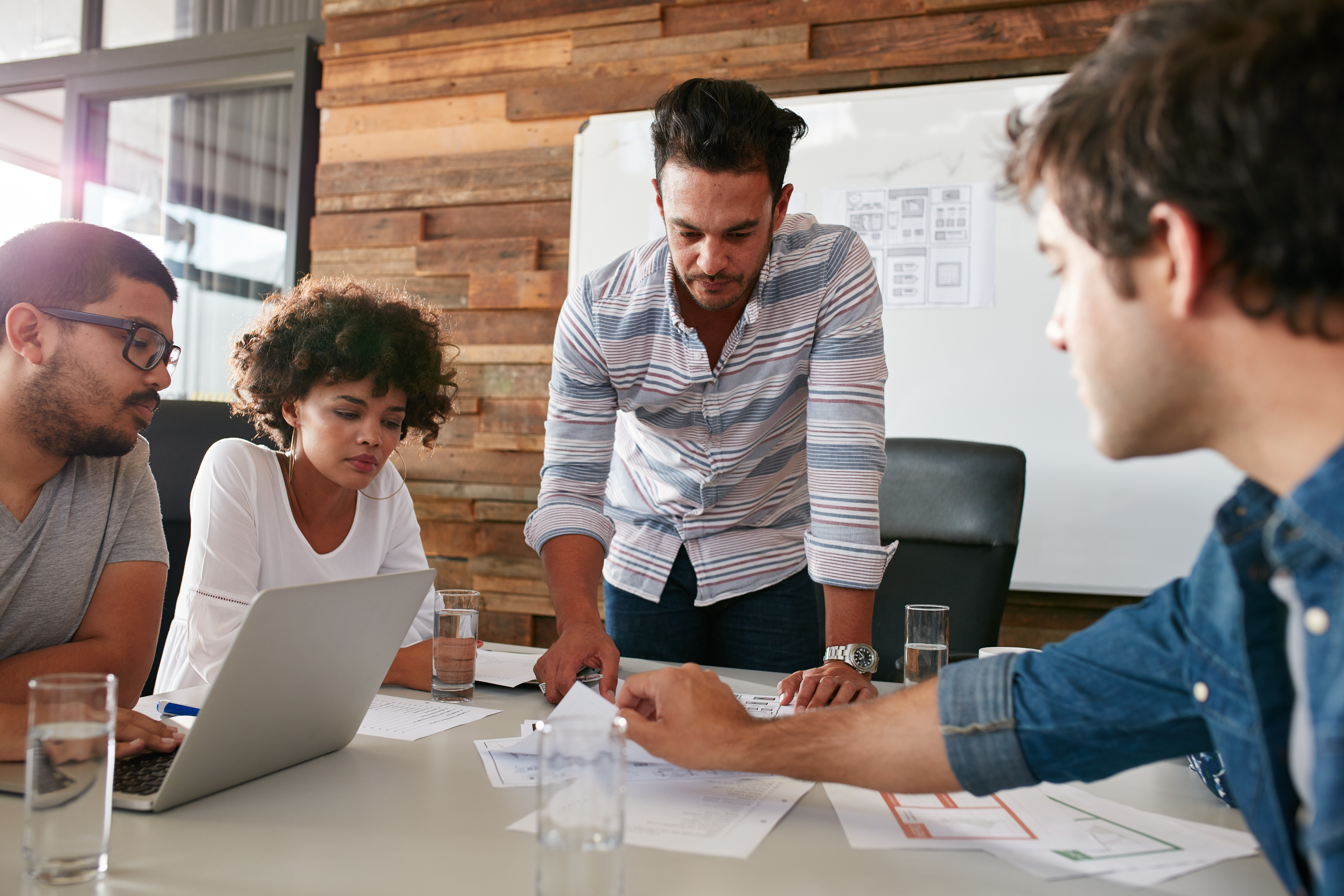Four people are gathered around an office table looking at papers during a Digital Marketing meeting.